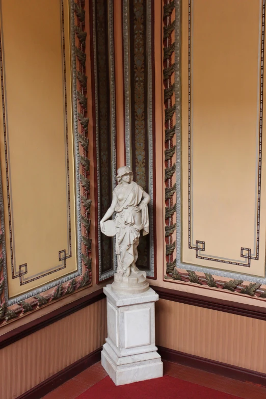 a statue in front of ornate gold wallpaper and an area with red carpet