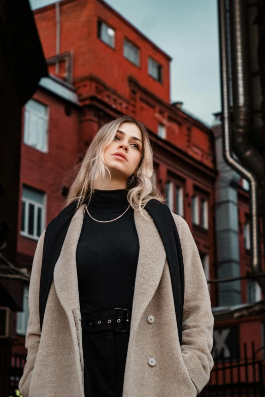 a woman standing outside of a red brick building with her hands in her pockets