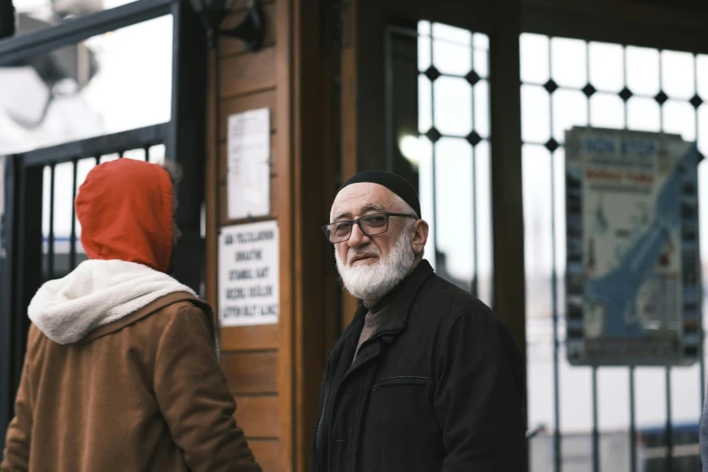 a man with a white beard in the background has a person with a red scarf