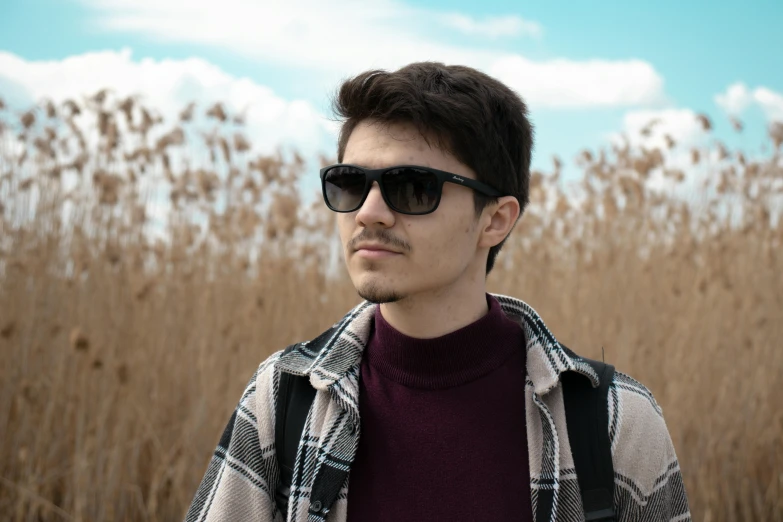 man wearing black sunglasses in front of tall grass