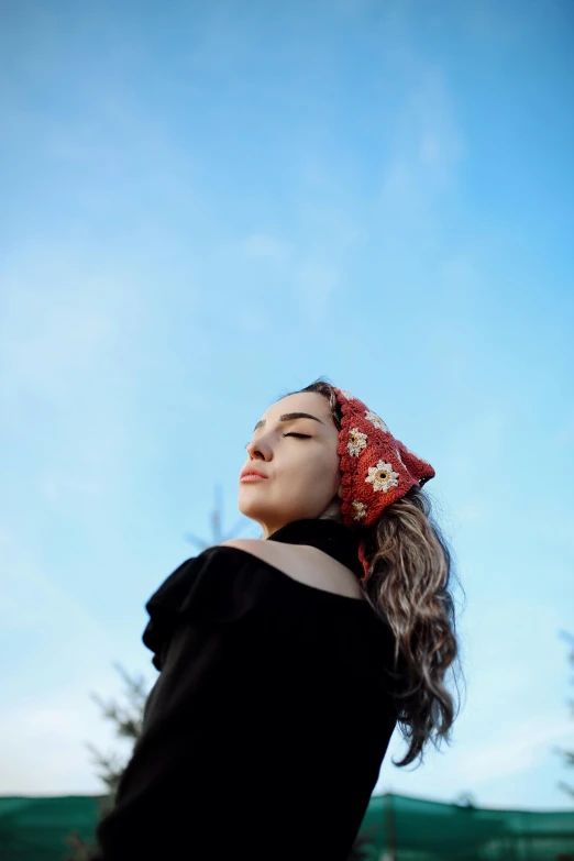 a woman in black shirt and head scarf looking up at blue sky