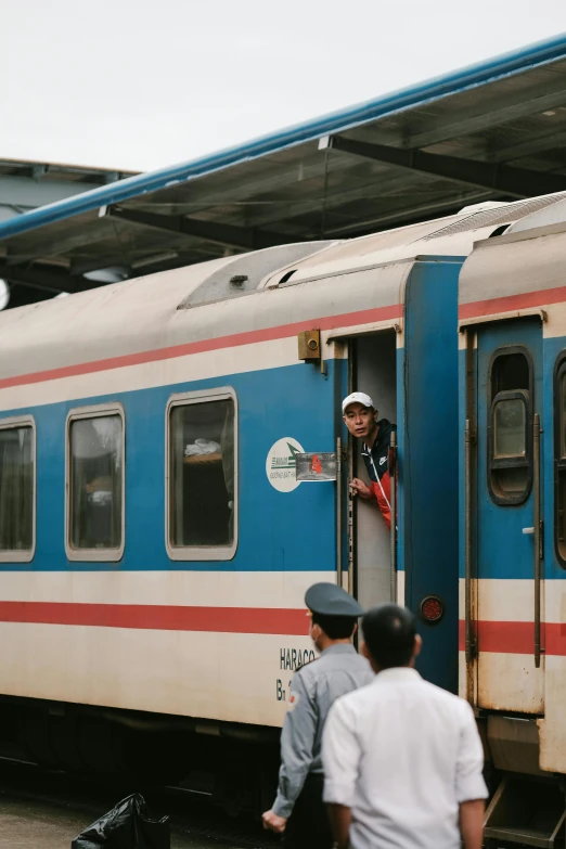 a man with a hat on and a blue and white train in the background