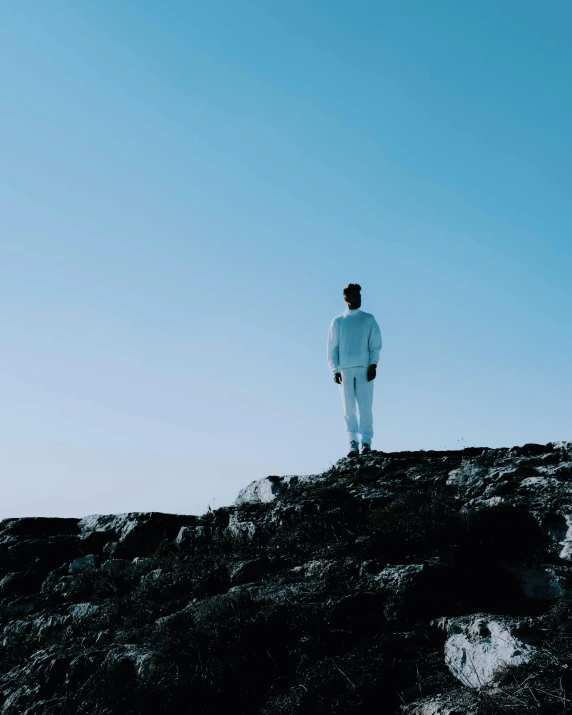 a man stands on top of a rocky hill looking off into the distance