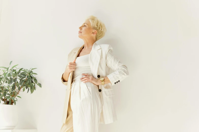 an older woman in white clothes standing against a wall with her arms on her hips