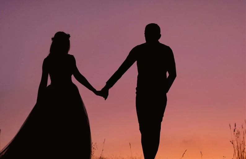 silhouettes of two people standing holding hands with one another