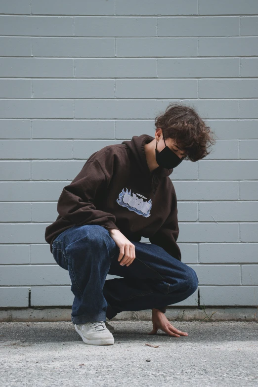 a man in jeans crouches down near a grey wall