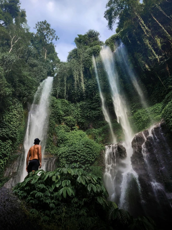 a young man stands on a rock looking at a waterfall