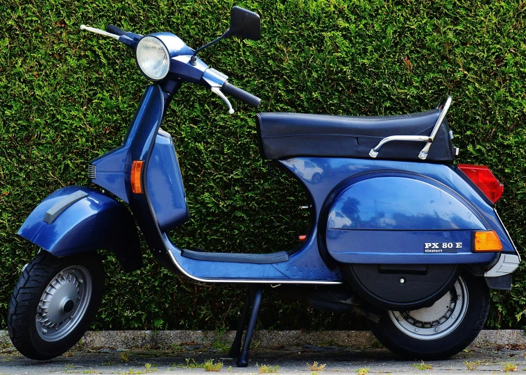 a blue scooter parked on the street near a hedge