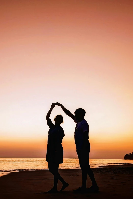 two people stand on the beach and pose at sunset