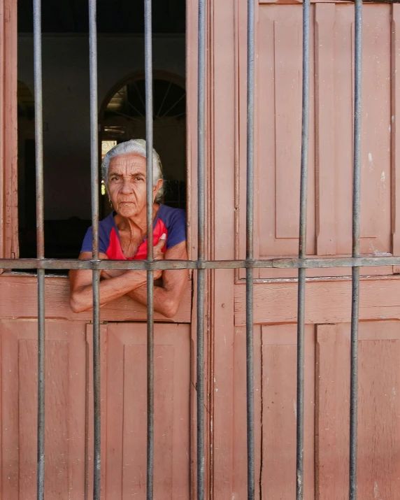 a man in red shirt looking out from window behind bars