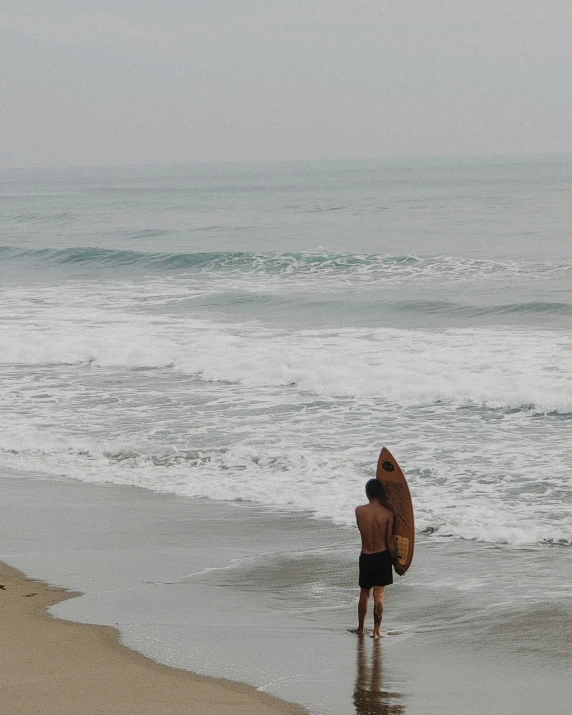 the man stands in shallow water as he holds his surfboard