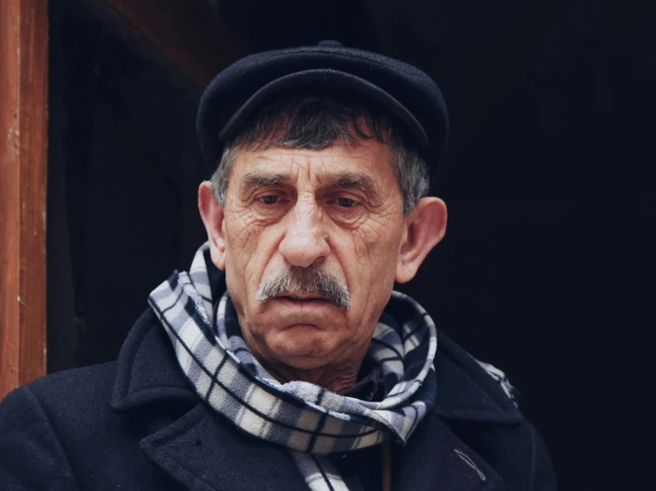an old man looking down with a hat and scarf on