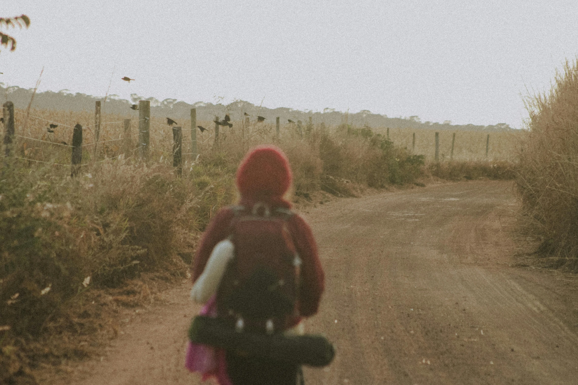 a woman in a red coat and boots riding a bike down a dirt road