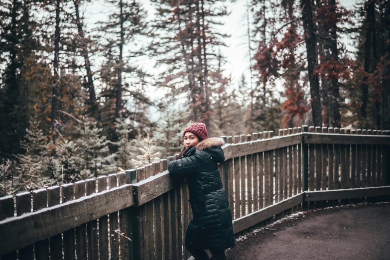 a woman in winter clothing stands on a walkway next to trees