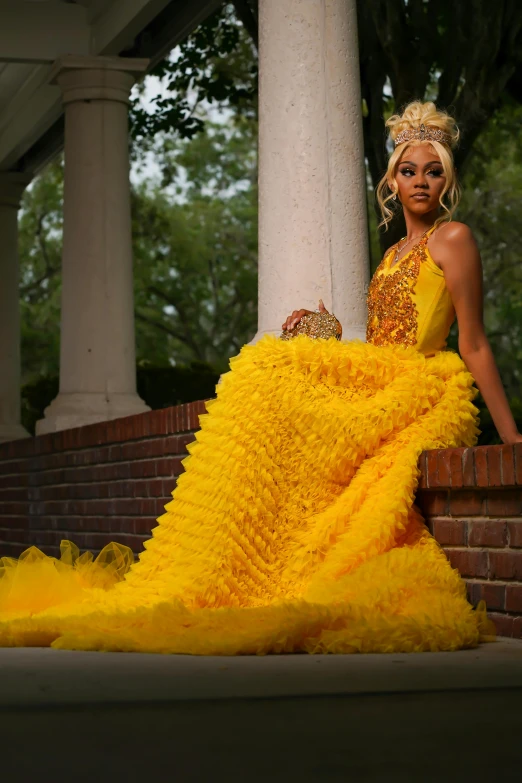 a woman in a yellow gown standing in front of an old brick building