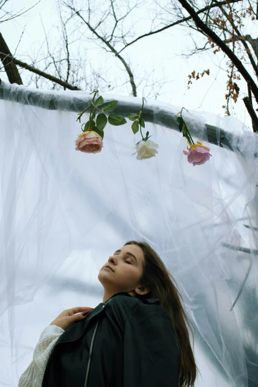 there is a woman with her eyes closed looking up at flowers in a net