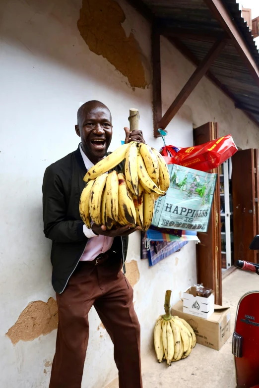 a man holding large bunches of bananas near a building