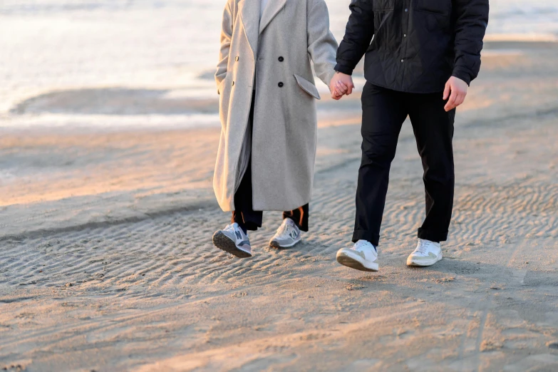 a couple holds hands walking along the beach