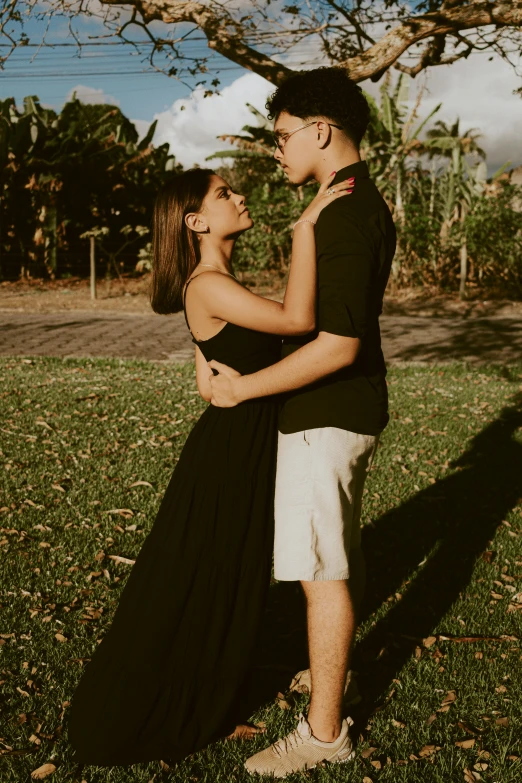 young woman and man stand next to each other in front of a tree