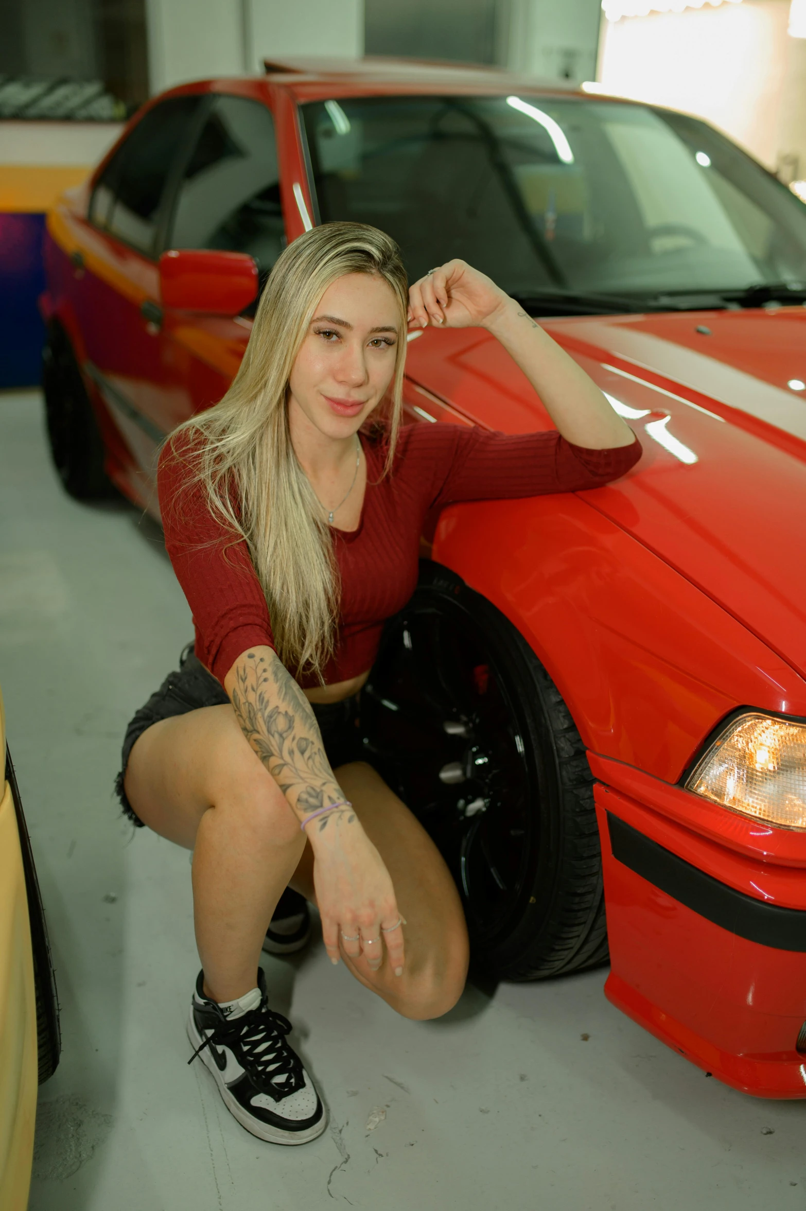 girl with tattoos posing in front of a red bmw