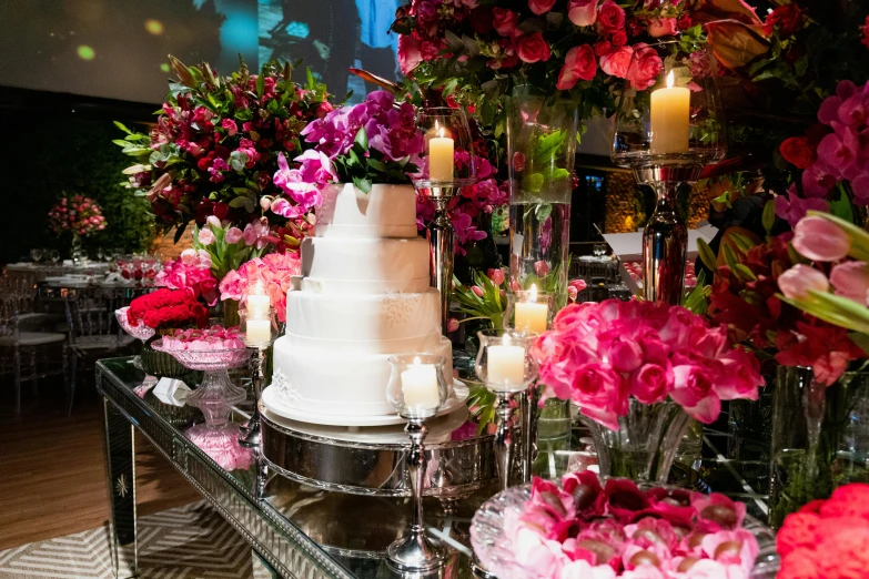 wedding cake surrounded by flowers and candles on a glass table