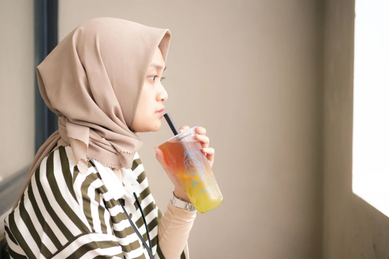 a person drinking a glass of beverage while standing next to a window