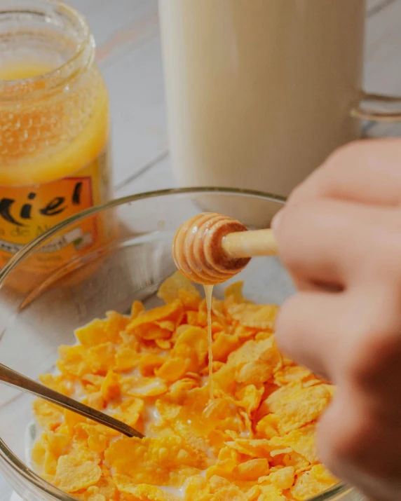 a bowl of cereal with a hand squeezing honey into it