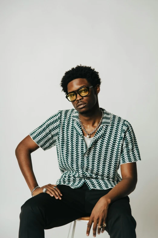 man with sunglasses on, sitting on white stool