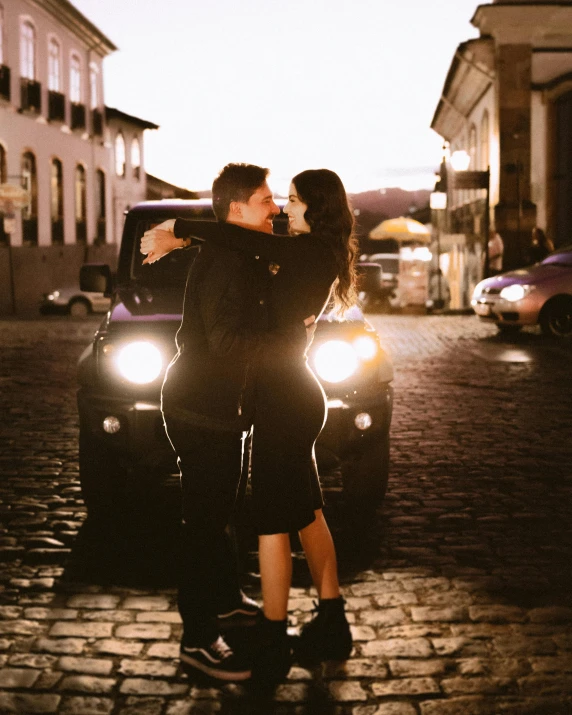 two people standing in front of a car with their hands around each other