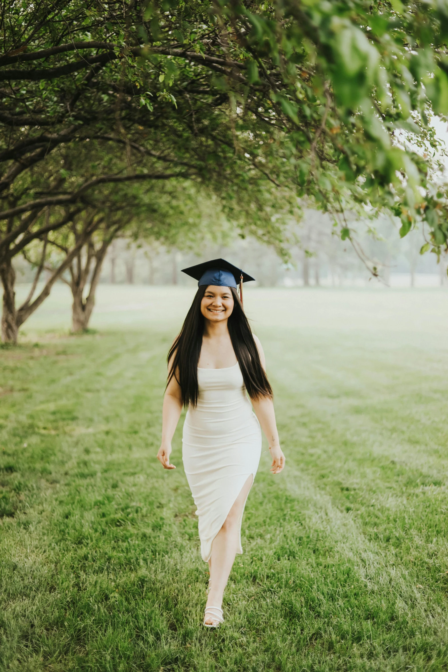 woman in graduation dress walking through field under trees