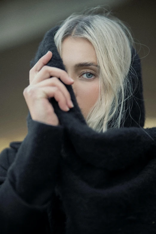 blonde female with blue eyes and black hoodie holding onto her jacket