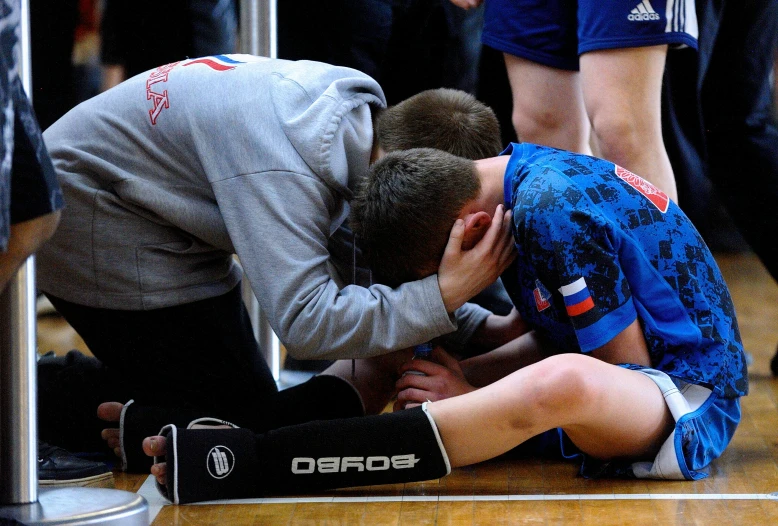 a boy is kneeling on the floor with a teammate