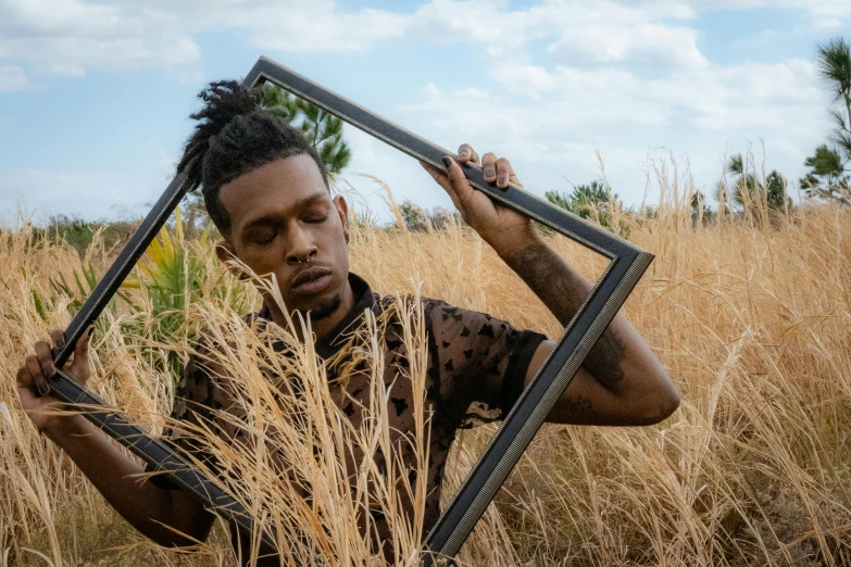 a man standing in a field holding up a mirror