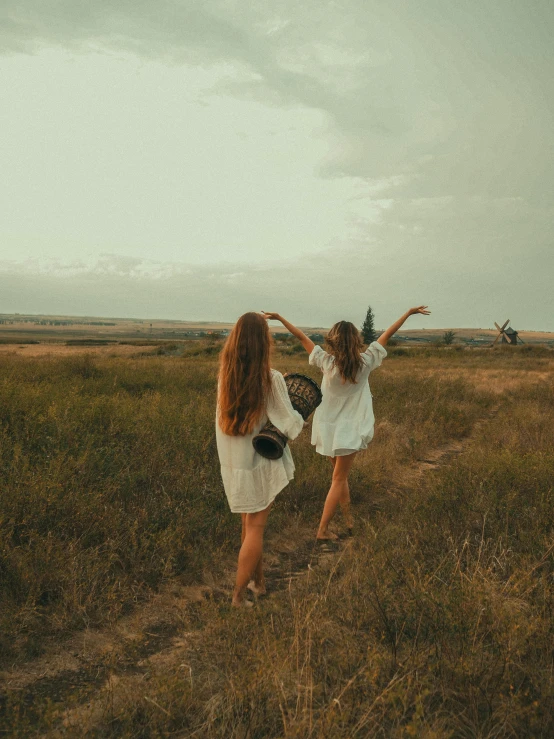 two little girls walking in a field holding a tennis racket