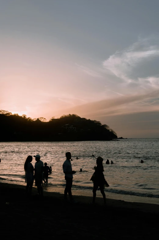 silhouette of several people walking along beach during sunset