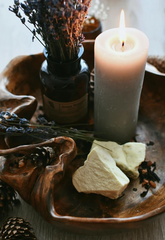 a lit candle is next to some dried flowers on a wooden tray