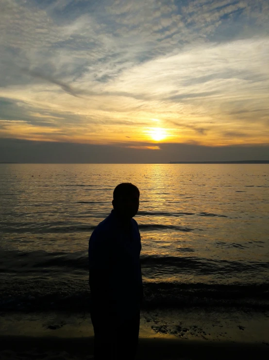 a person is standing on the edge of the ocean while the sun goes down