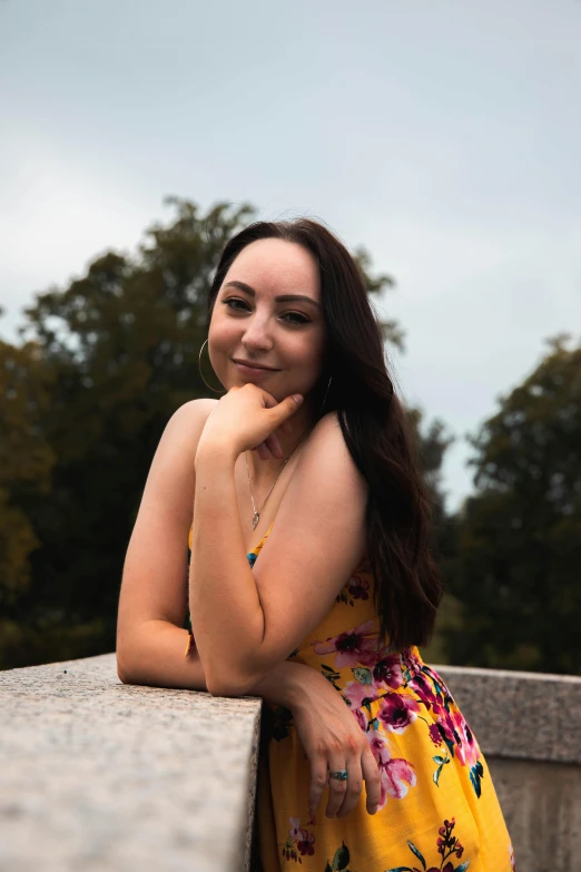 a girl in a yellow dress sitting next to the edge of a stone wall