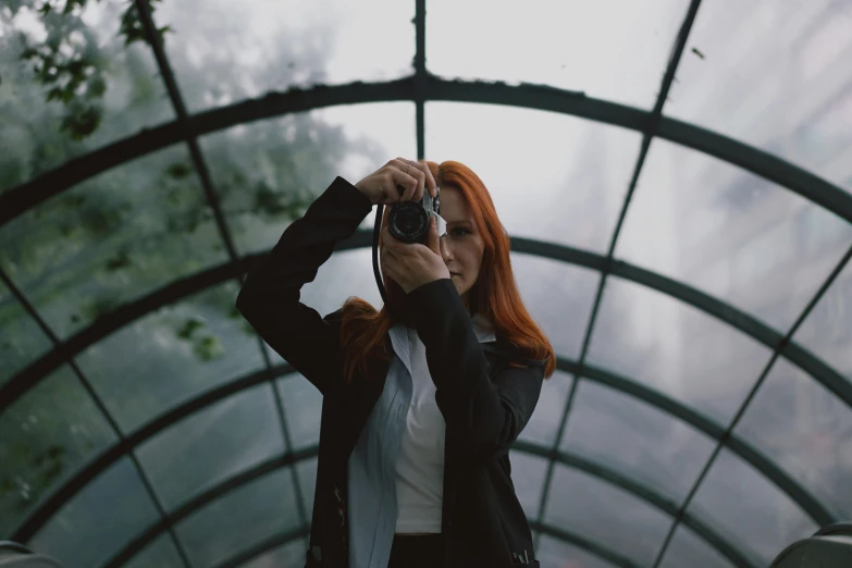 a woman holding a camera taking a po in front of a glass structure