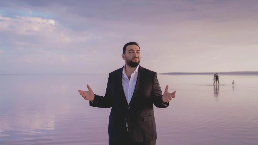 man in suit standing on the ocean with his hands open