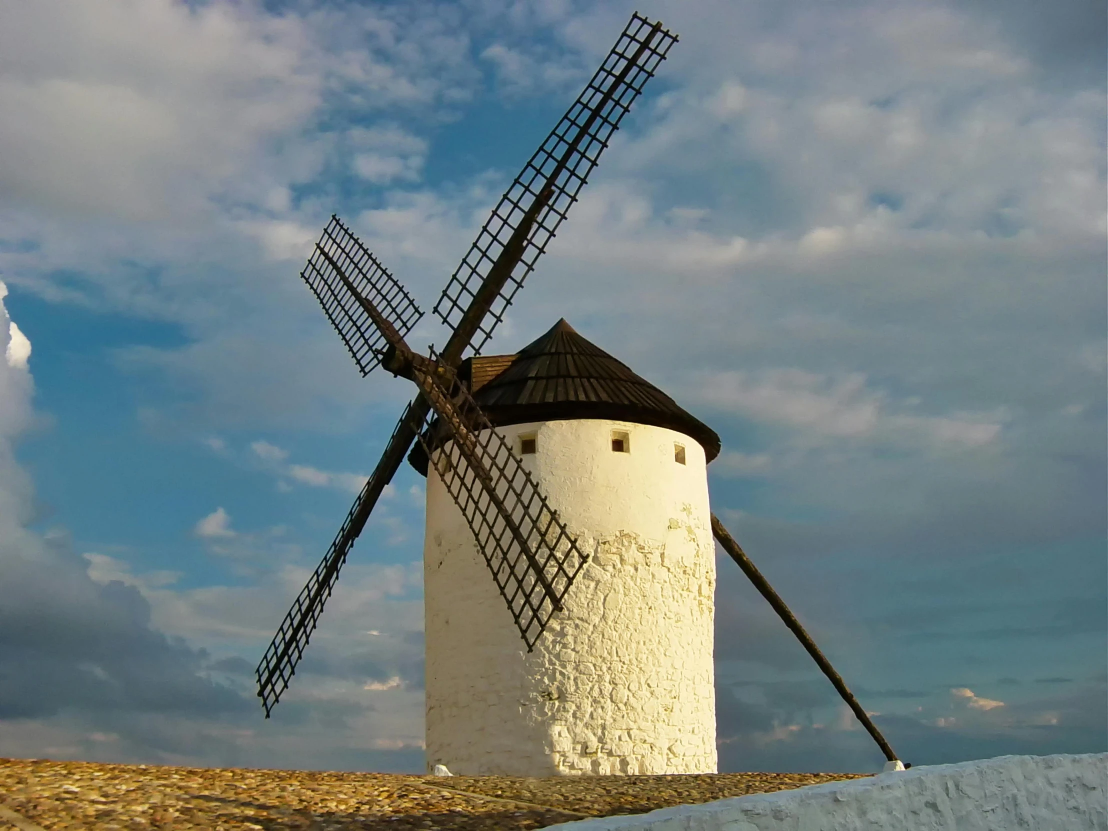 a windmill on a hill, under a blue cloudy sky