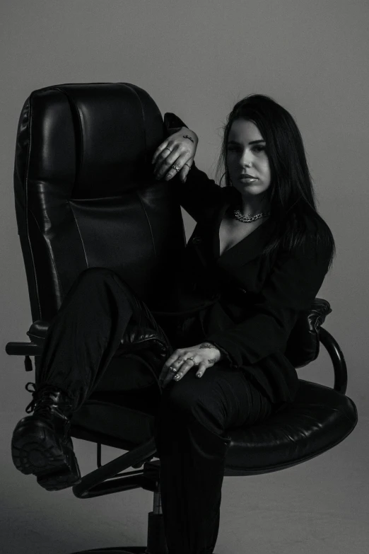 a woman in a black suit sitting on a chair with a arm folded