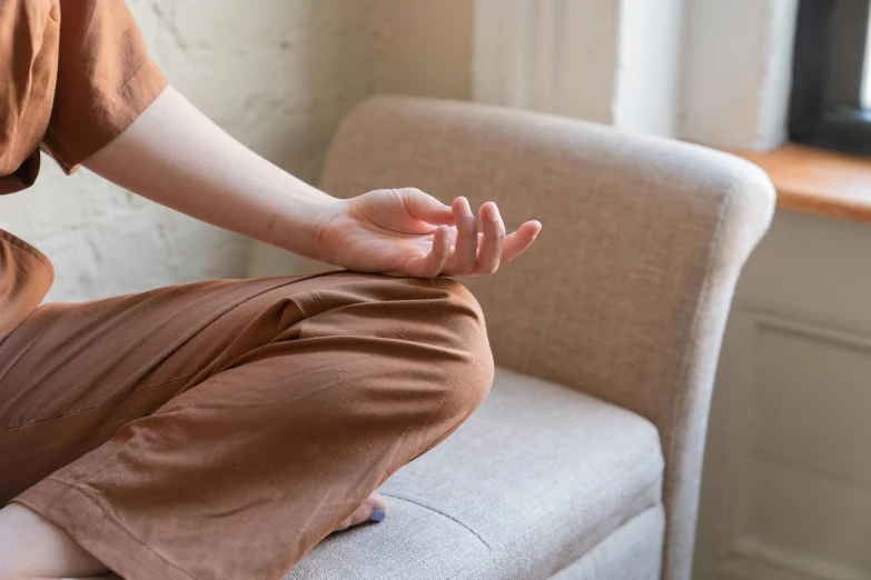 a woman sits on a couch in front of a window, doing yoga