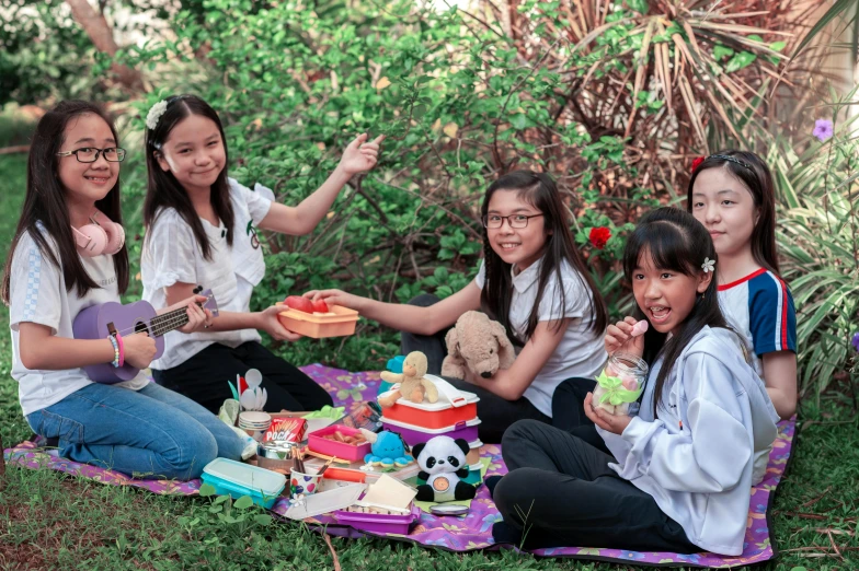 four girls sitting on the ground holding their lunch boxes