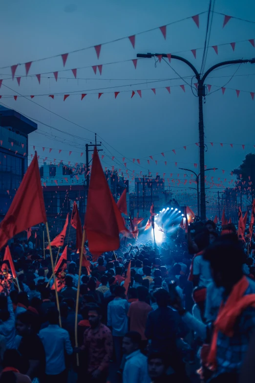 an open air area with a group of people, a stage, and some red flags