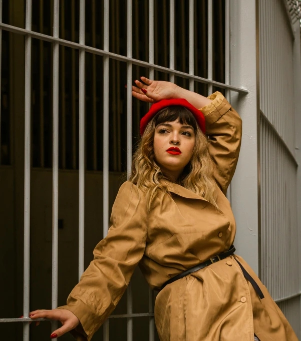 a woman in a tan coat and red hat standing next to a metal fence