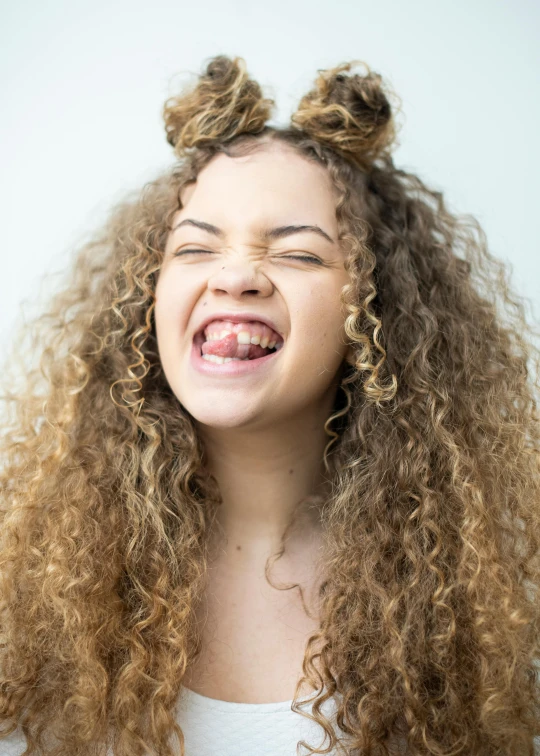 a smiling girl with curly hair has her eyes closed