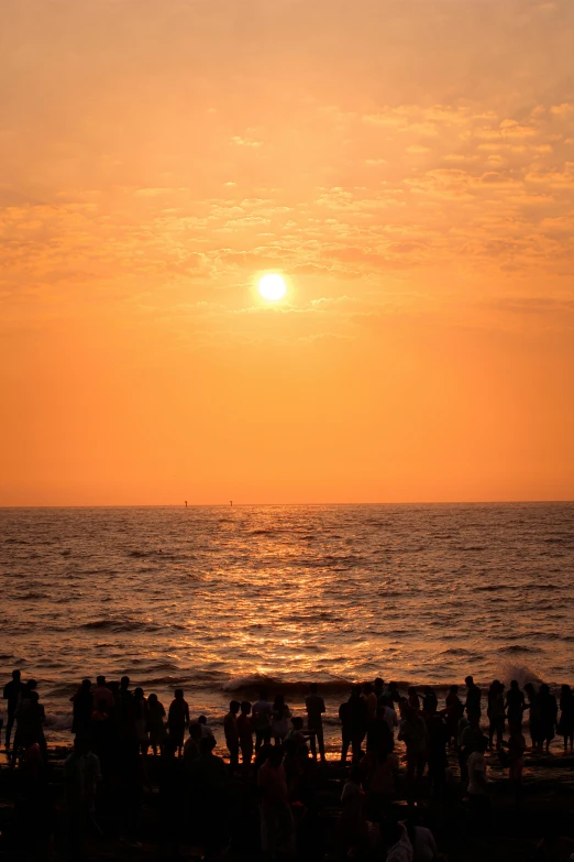 several people are on the beach as the sun sets