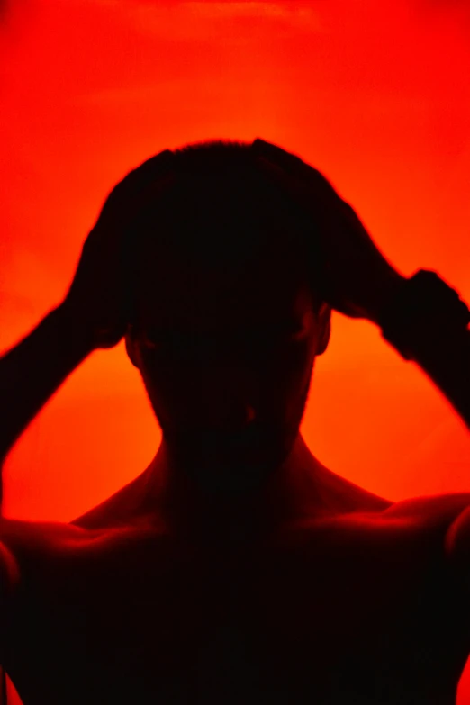 a man with a red background holding his hands to his hair