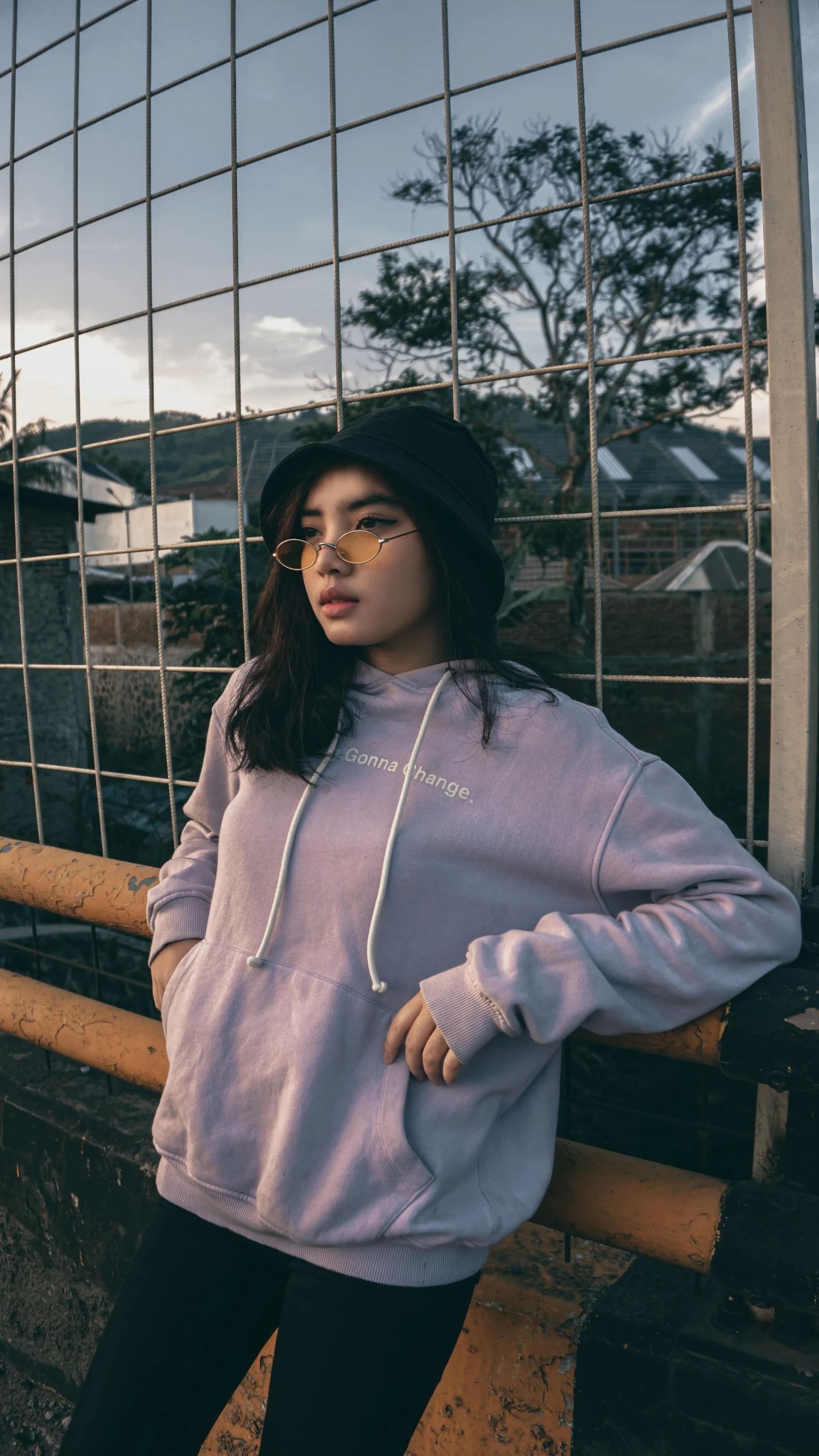 a woman leaning against a fence while wearing a pink sweatshirt